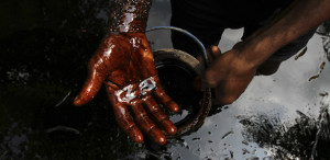 A man samples crude oil at the bank of a polluted river in Bidere community in Ogoniland in Nigeria's delta region